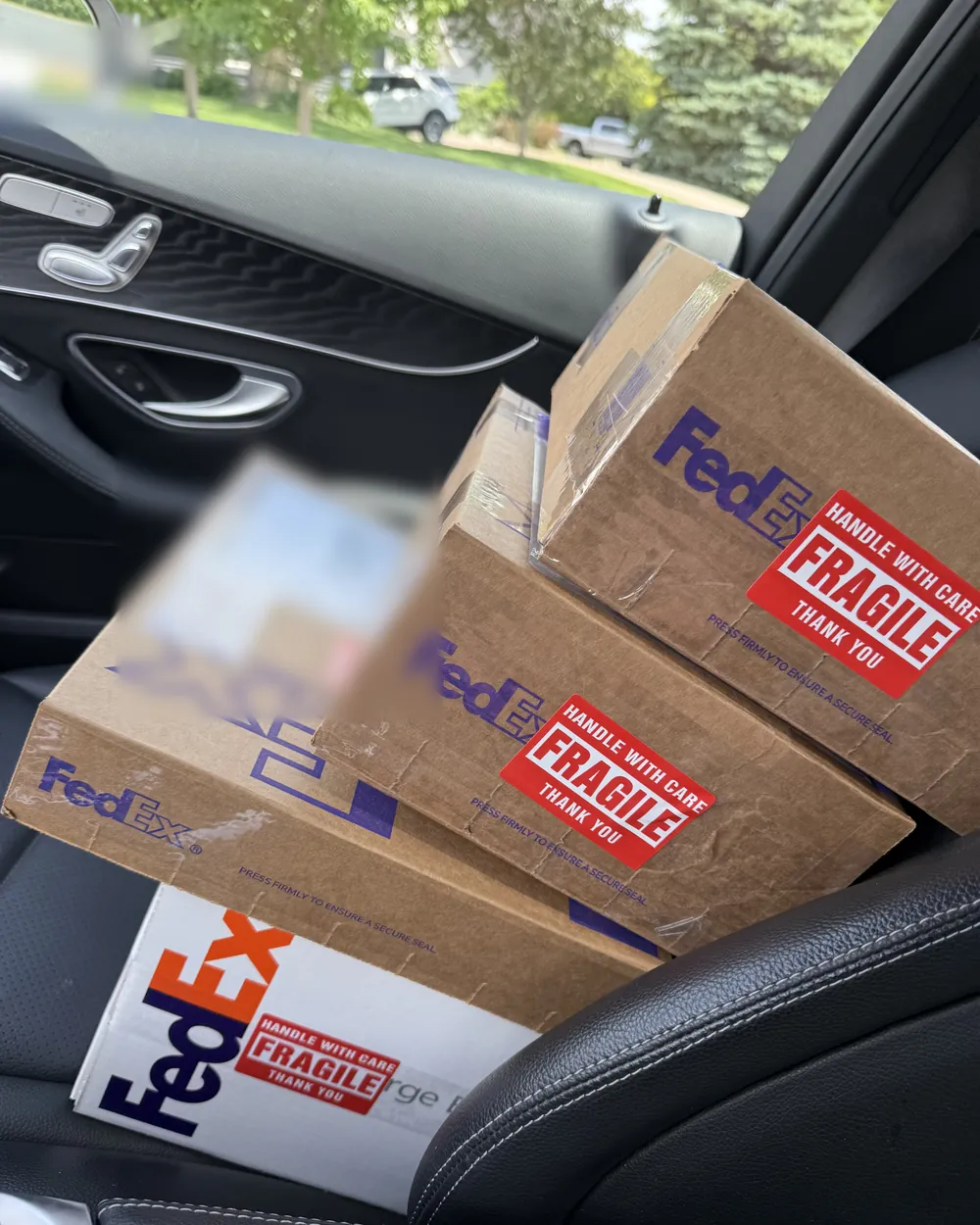 Four taped and fragile-stickered shipping boxes stacked on a car's passenger seat, on their way out for insured delivery